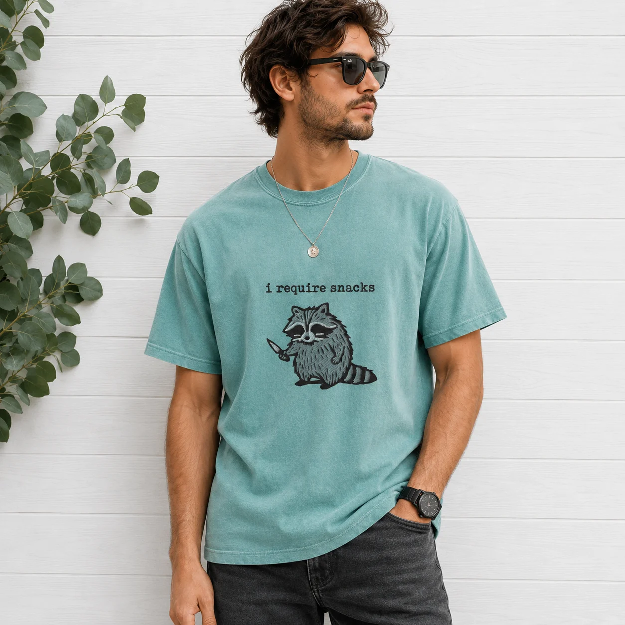 Man wearing green t-shirt with I Require Snacks raccoon design
